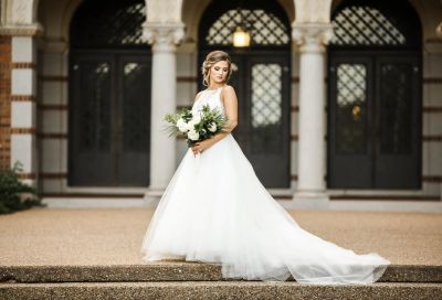 Bride in a lace wedding gown standing outside a classic Denton County building
