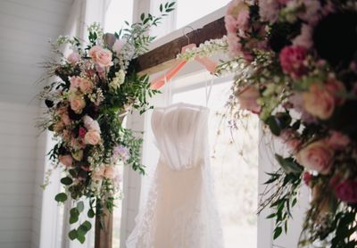 Beautiful floral arrangement with pink roses and greenery next to wedding dress, showcasing the artistry of professional wedding florists