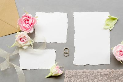 Blank wedding invitation cards with pink paper roses, ribbon, and a kraft envelope