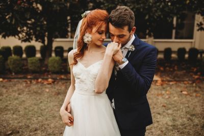 Groom in a navy suit kissing his bride's hand at an outdoor Denton-area wedding
