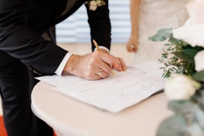 Close-up of a groom signing official marriage documents at a small table